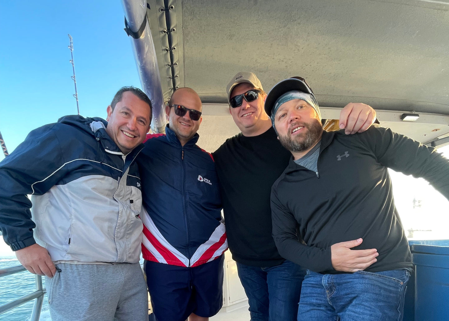 Five people posing together on a boat with a clear blue sky in the background.
